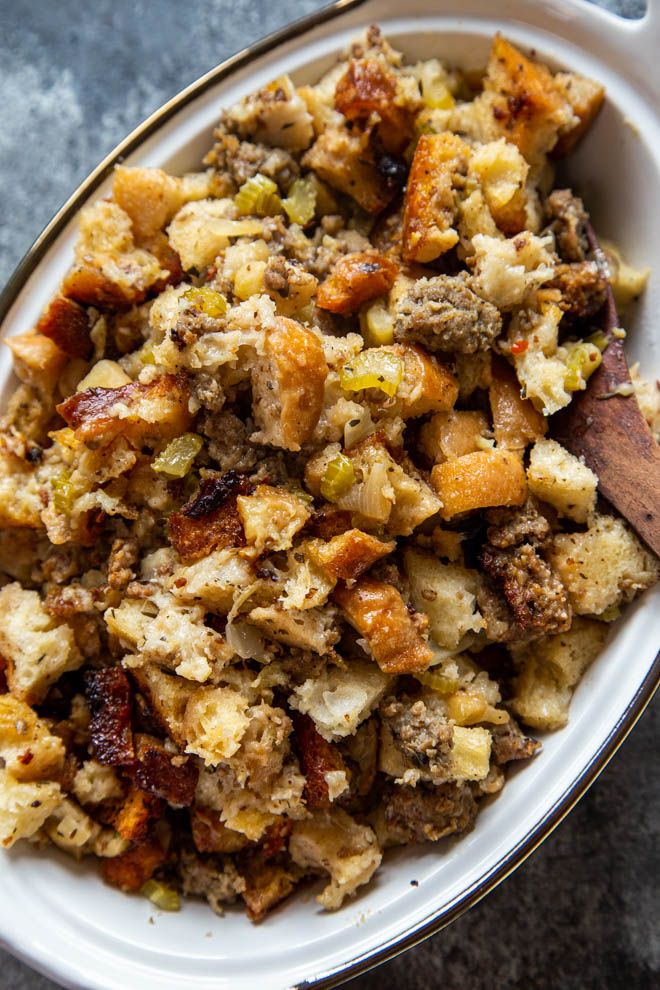 a white bowl filled with stuffing on top of a table next to a wooden spoon