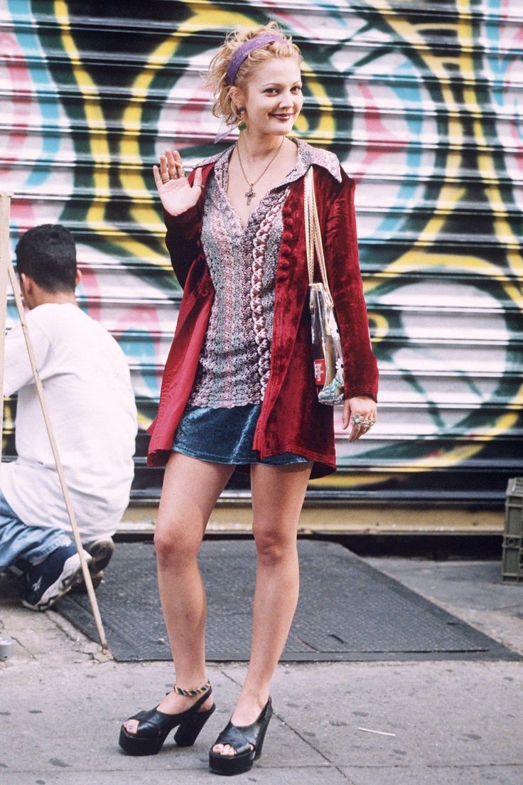 a woman standing on the sidewalk in front of a graffiti covered building with her hand up