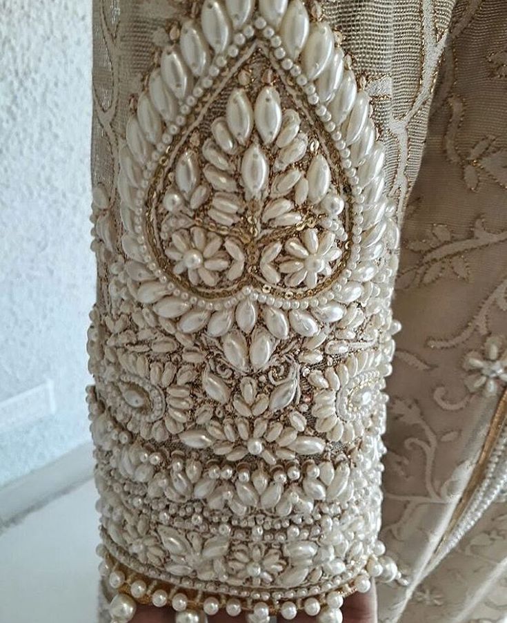 a close up of a person's hand holding a white beaded curtain with pearls on it