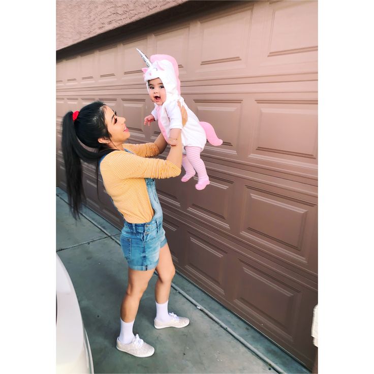 a woman holding a baby in front of a garage door with a unicorn on her head