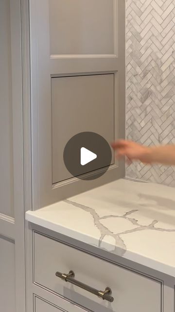 a person is pointing at the counter top in a kitchen with gray cabinets and white marble