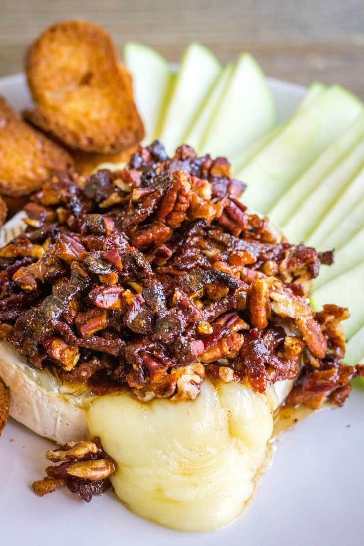 baked brie with pecans and bacon on a white plate next to apple slices