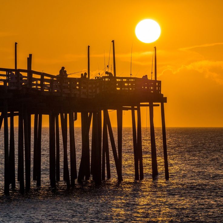 the sun is setting over an ocean with a pier in the foreground and people sitting on it