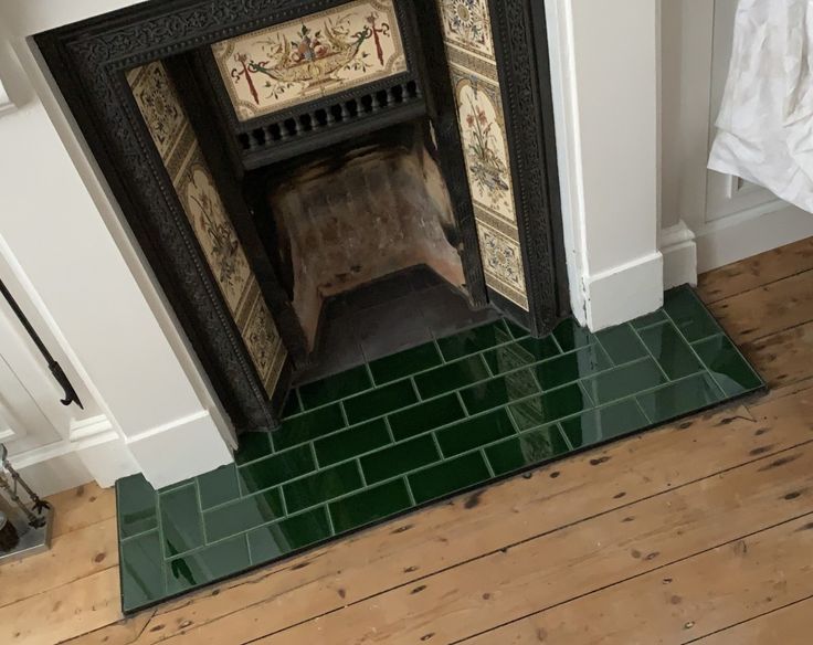 a fireplace with green tiles on the floor next to a white wall and wooden floors