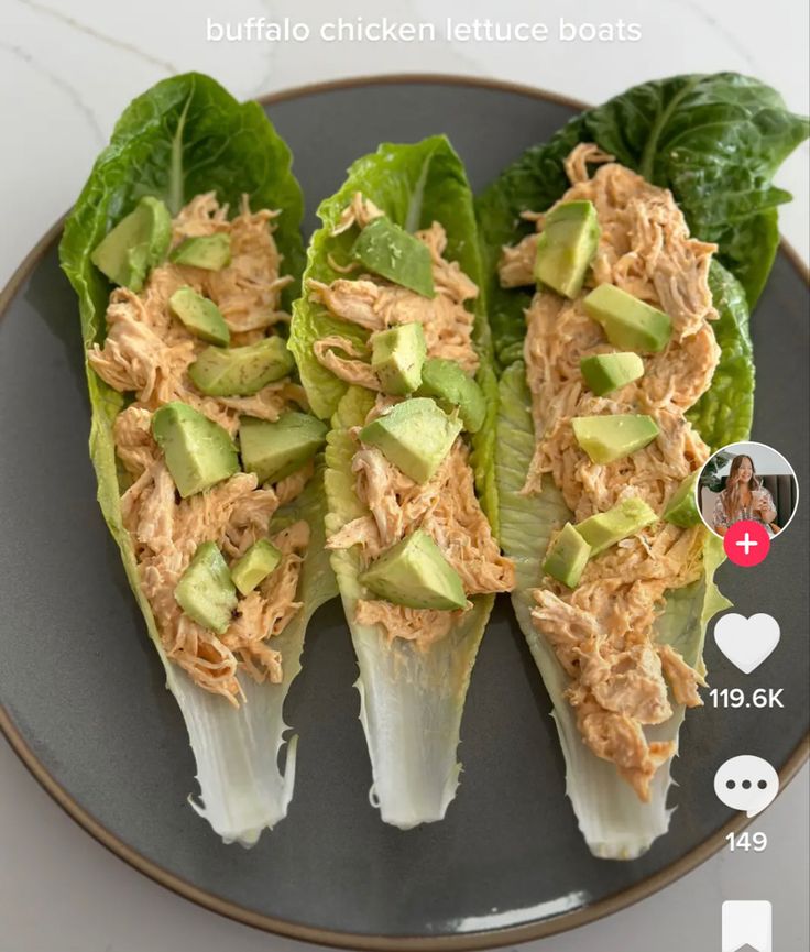 three lettuce wraps with shredded chicken and avocado on top, sitting on a black plate