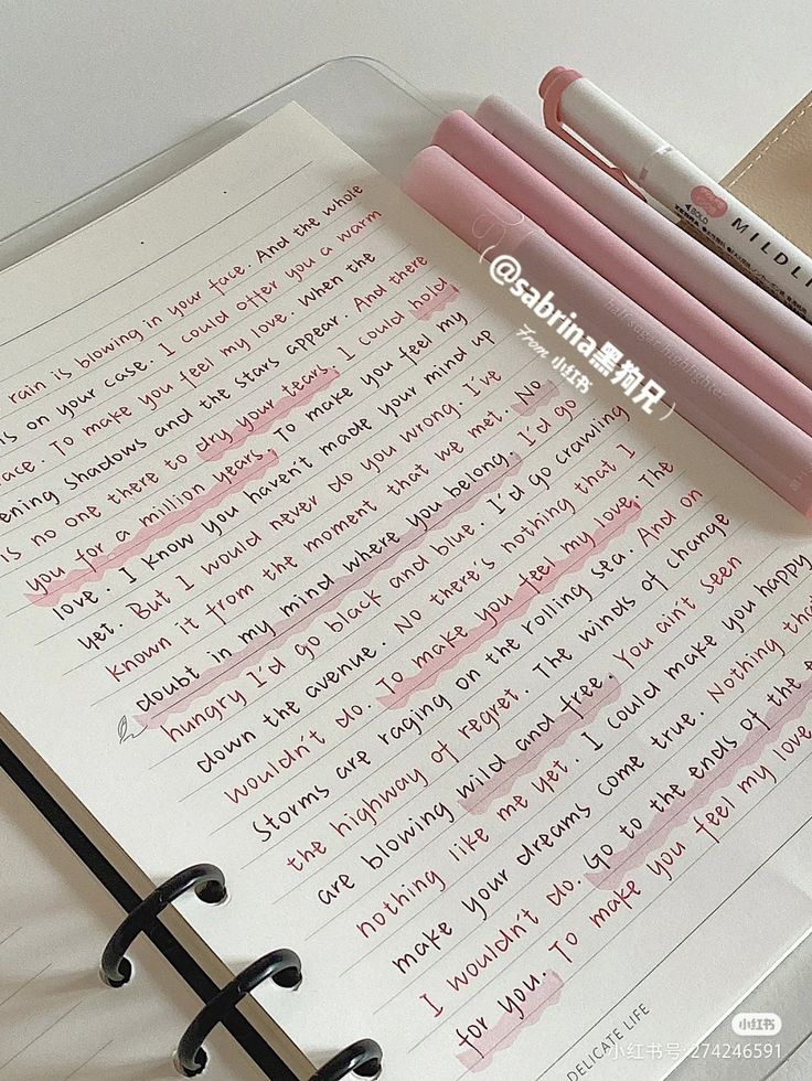 three pink pens sitting on top of an open notebook next to some other writing implements