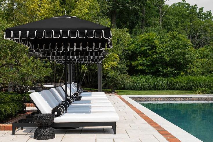 a row of white couches sitting next to a swimming pool with an umbrella over it