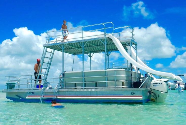 two people standing on the top of a boat in the water with a slide going down it