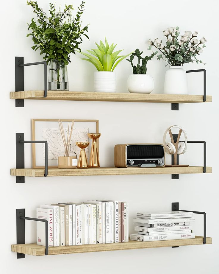 two wooden shelves with books, plants and other items on them in front of a white wall