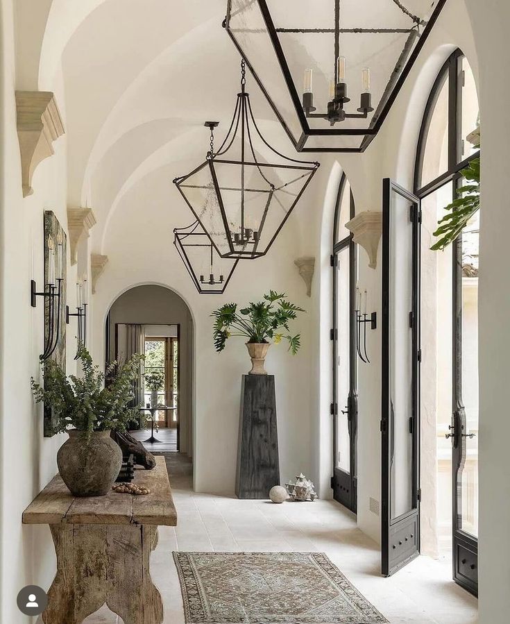 a hallway with an archway, potted plants and chandelier hanging from the ceiling