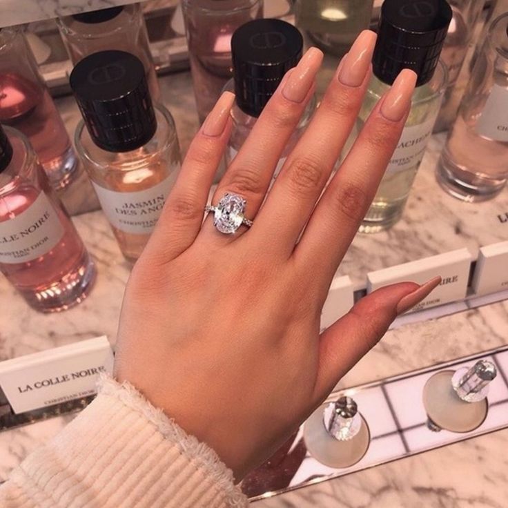 a woman's hand with a diamond ring on it in front of perfume bottles