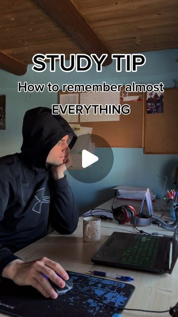 a man in a hoodie sitting at a desk with a laptop