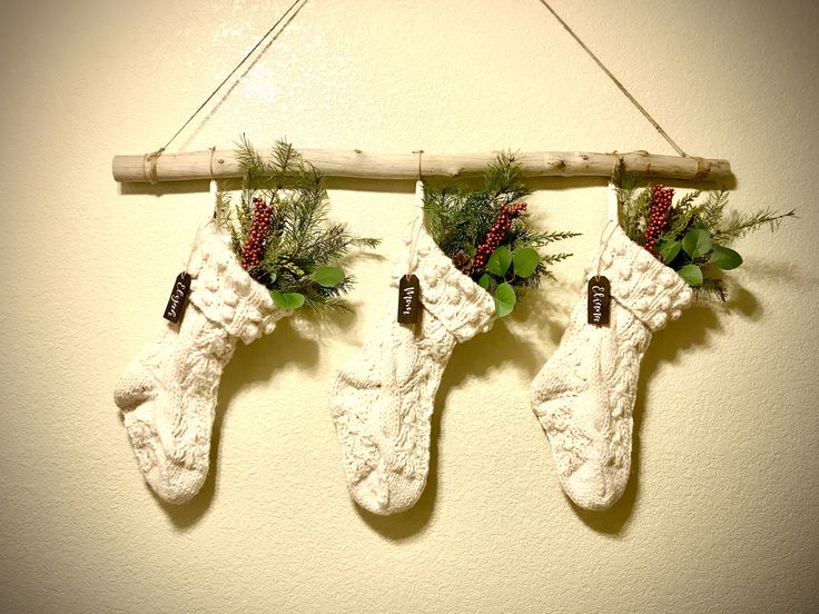 three christmas stockings hanging on a wall with greenery and pine cones attached to them