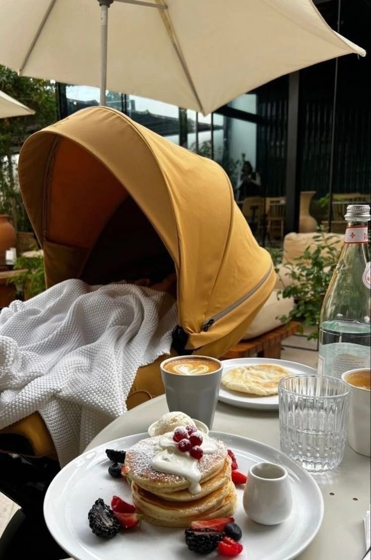 pancakes with berries and whipped cream are on a white plate under an umbrella next to a cup of coffee