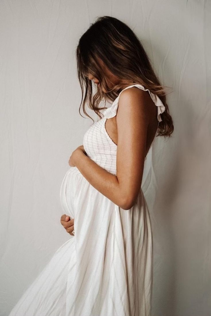 a pregnant woman standing in front of a white wall