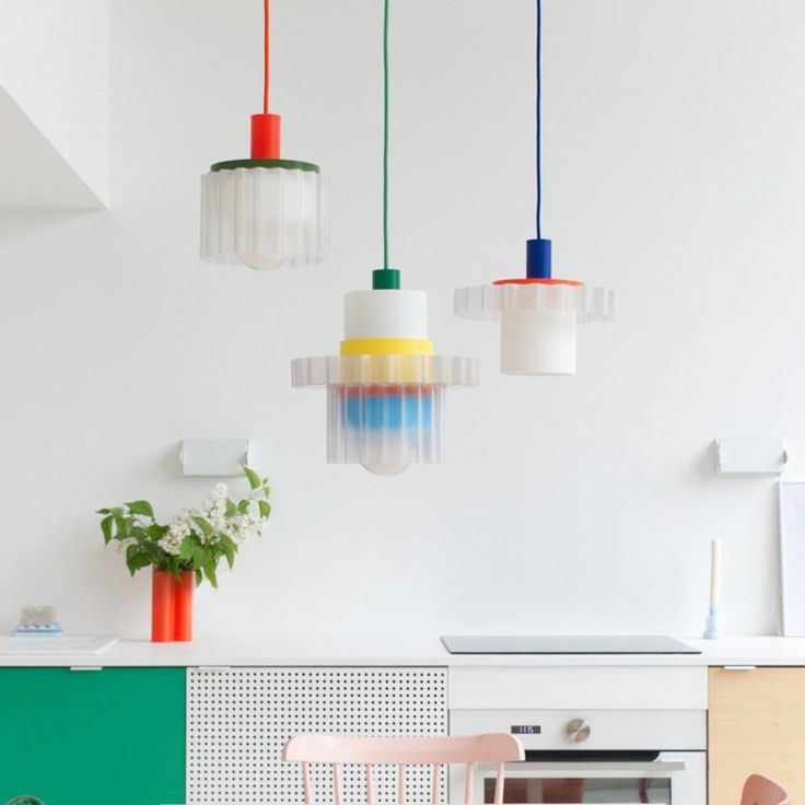 three colorful lights hanging from the ceiling above a kitchen table and chairs in front of an oven