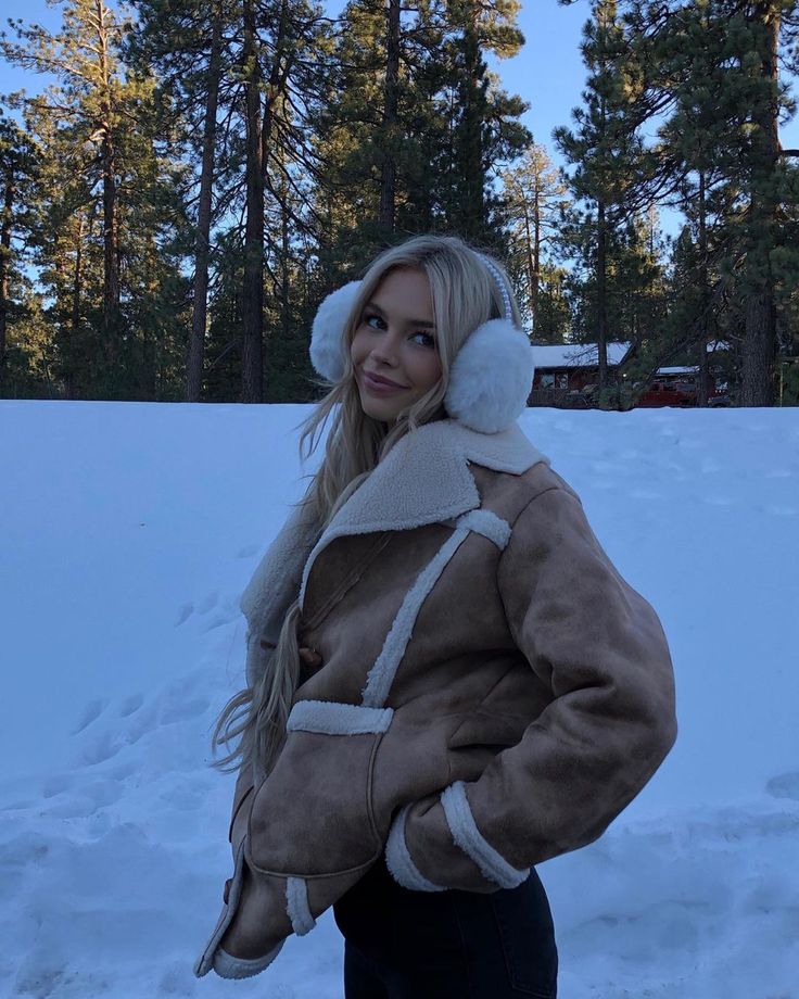 a woman standing in the snow wearing a jacket and hat with ear muffs on her head