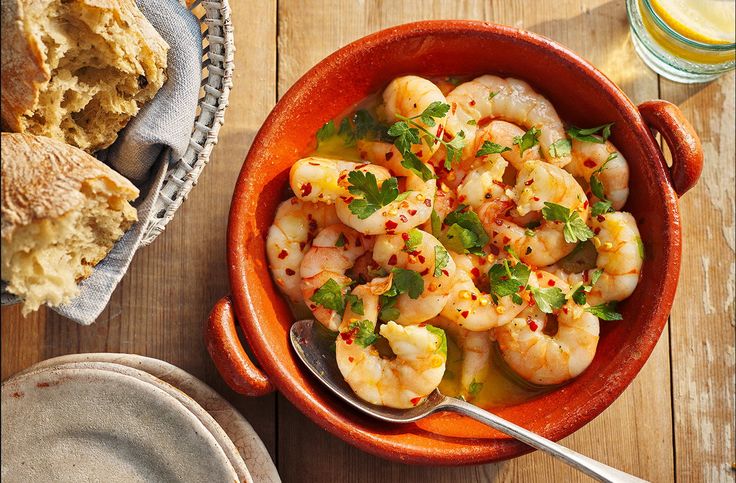 a bowl filled with shrimp and garnish next to a glass of orange juice