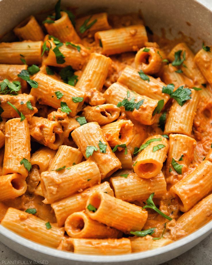 a white bowl filled with pasta covered in sauce and garnished with parsley