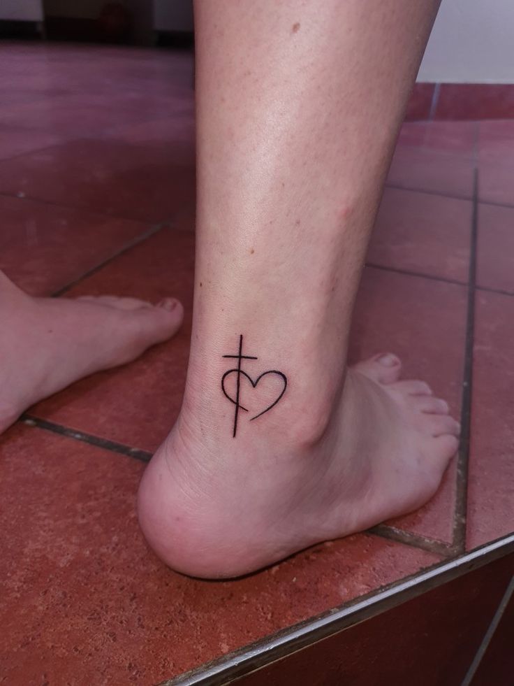 a woman's foot with a cross and heart tattoo on the bottom of it