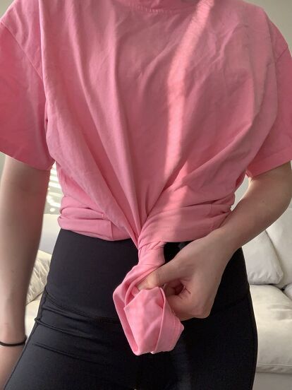 a woman wearing black pants and a pink shirt with a knot on the back of her top