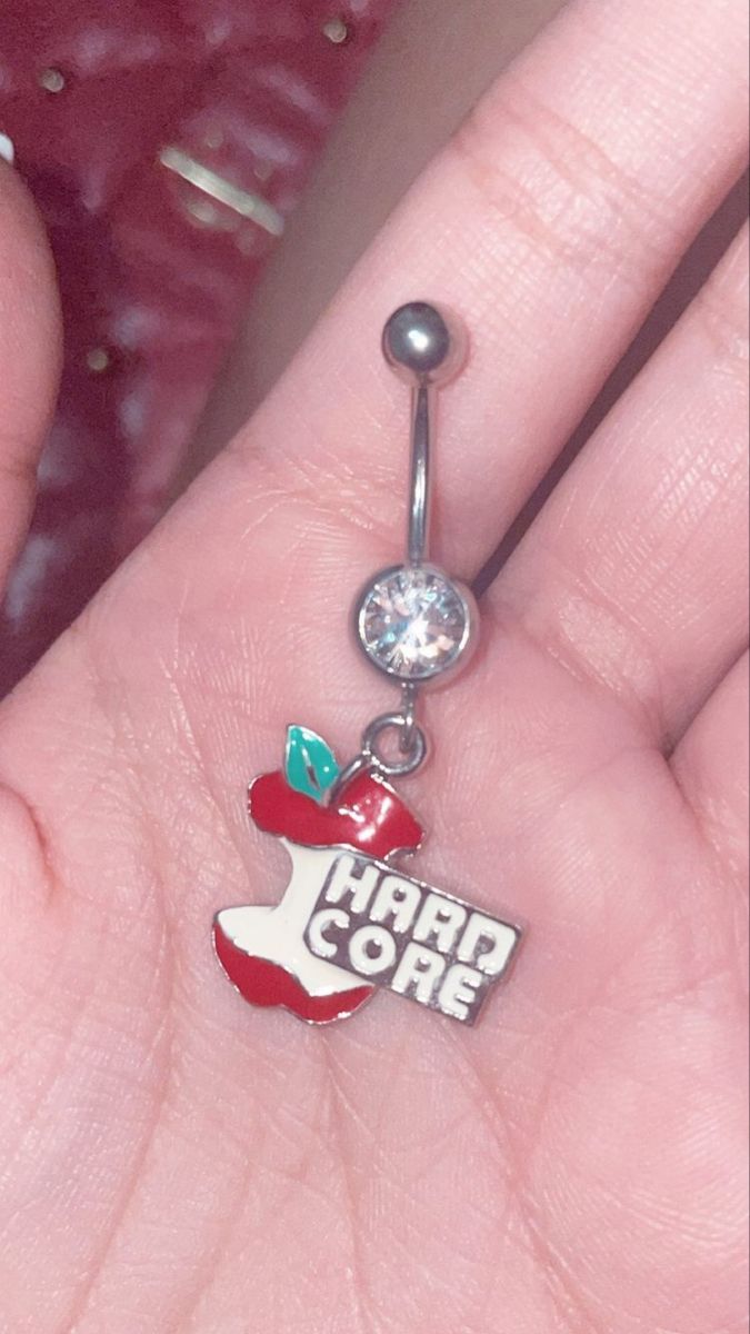 a person holding an apple belly ring with the word hard core on it's side