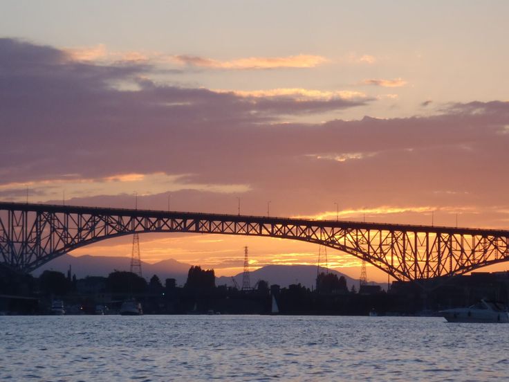 the sun is setting behind a bridge over water