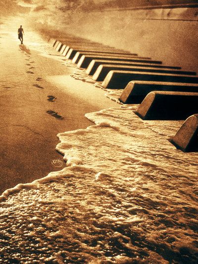 a person walking on the beach next to an old piano with footprints in the sand