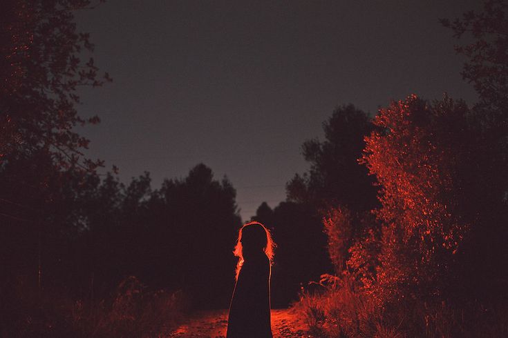 a woman standing in the middle of a forest at night with her back turned to the camera