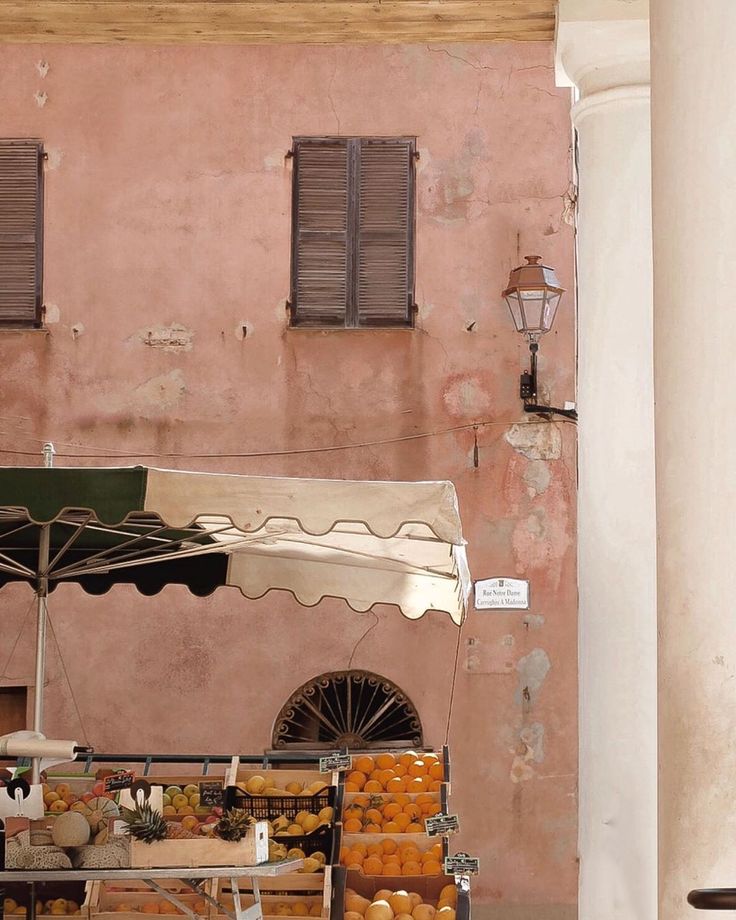 an outdoor fruit stand in front of a pink building