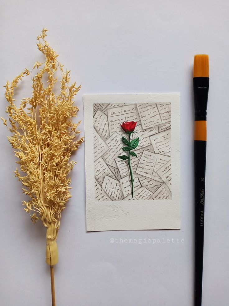 a red rose sitting on top of a piece of paper next to a paintbrush