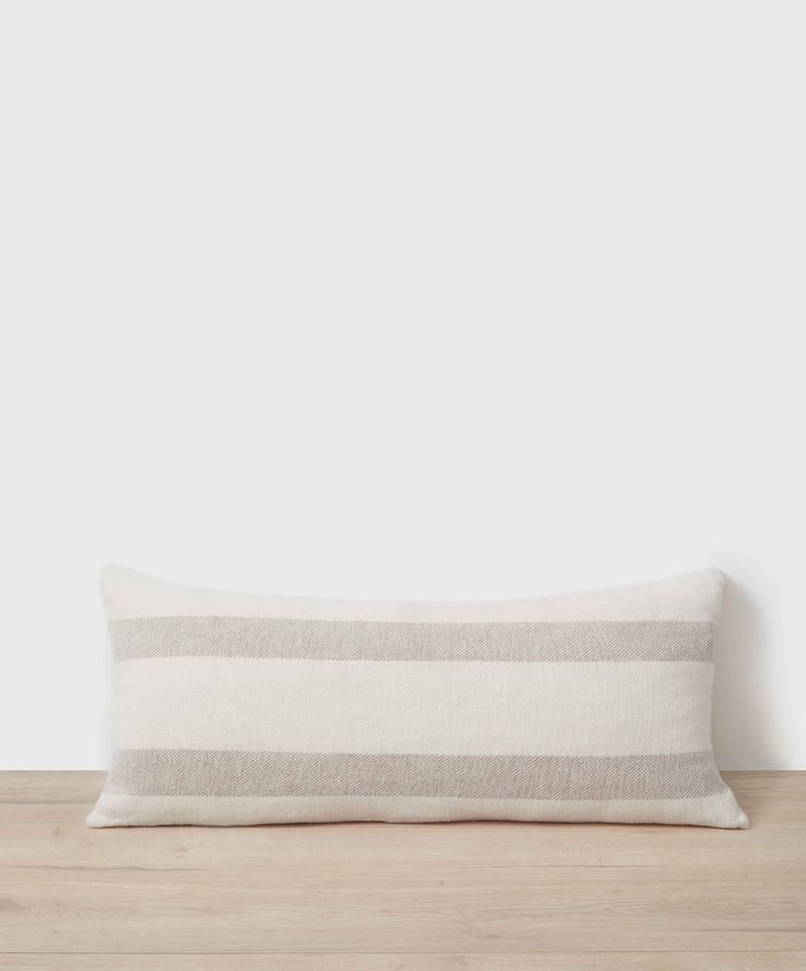 a white and grey striped pillow sitting on top of a wooden table next to a wall