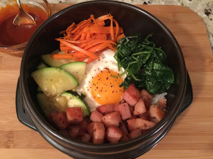 a bowl filled with meat, vegetables and an egg on top of a wooden cutting board