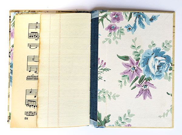 an open book with music notes and flowers on it's cover, sitting on a white surface