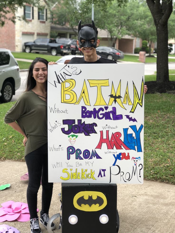 a man and woman standing next to each other in front of a sign with batman written on it