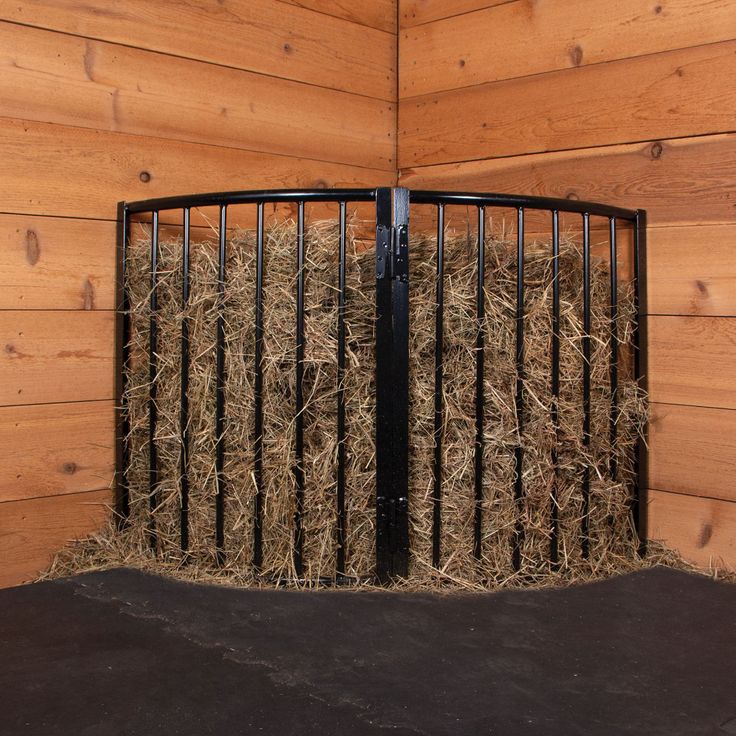 hay is stacked in the corner of a wooden room with black iron fence and wood paneling