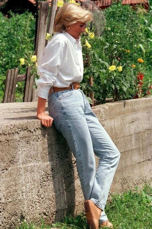 a woman leaning against a stone wall with her feet on the ground and wearing high heels