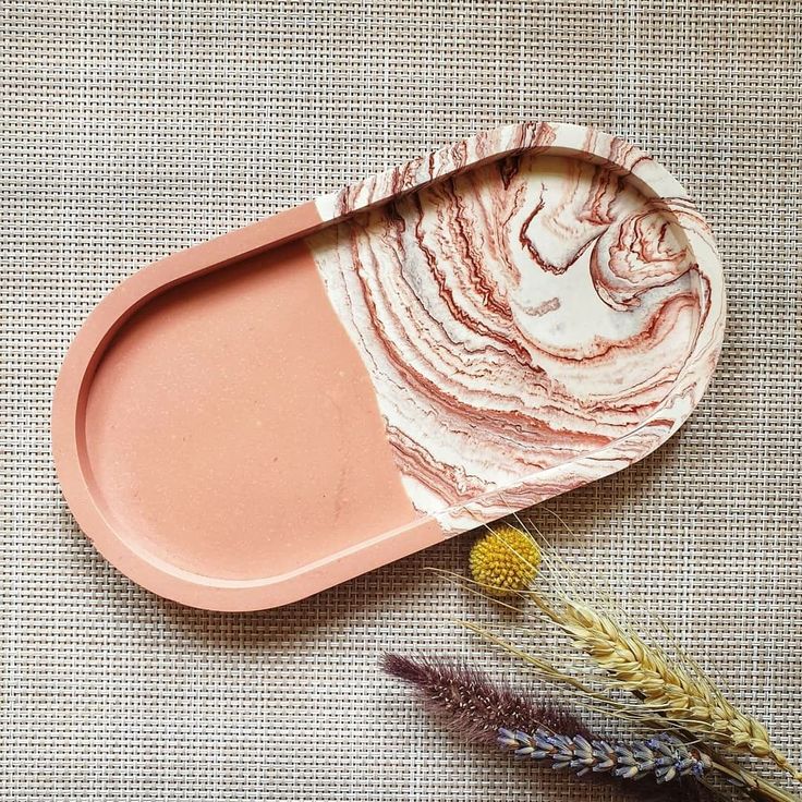 an oval plate with pink and white designs on it next to some dried flowers in the foreground