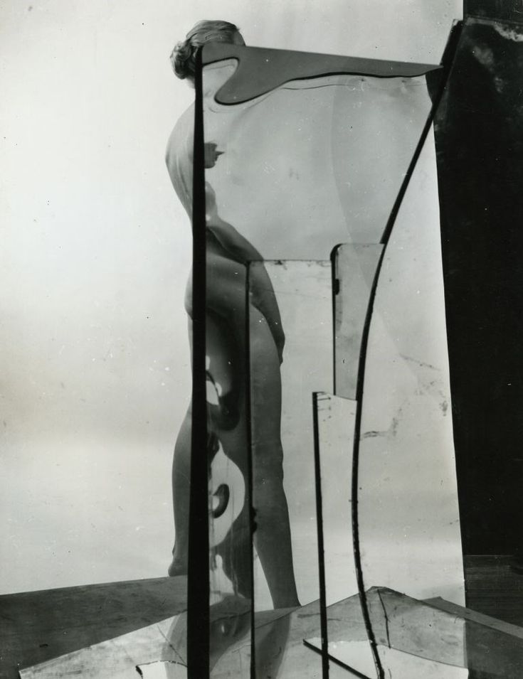 an old black and white photo of a man standing in front of a sculpture