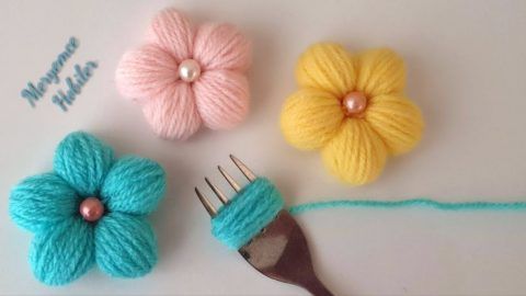 three crocheted flowers are sitting next to a fork and thread on a table