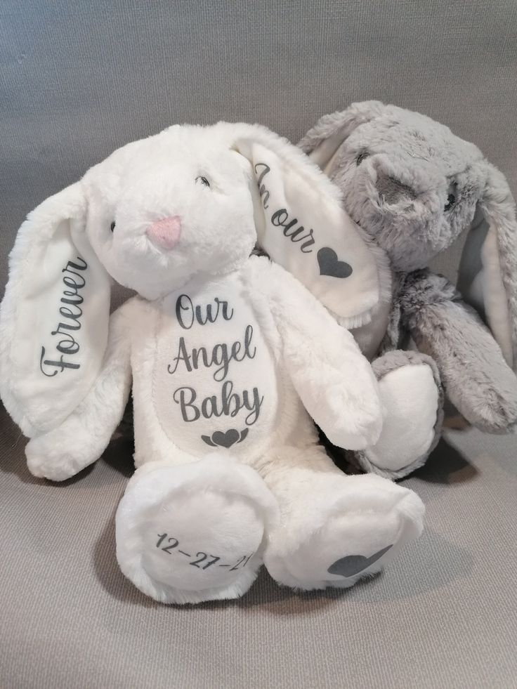 two stuffed animals sitting next to each other on a bed with the words our angel baby written on them