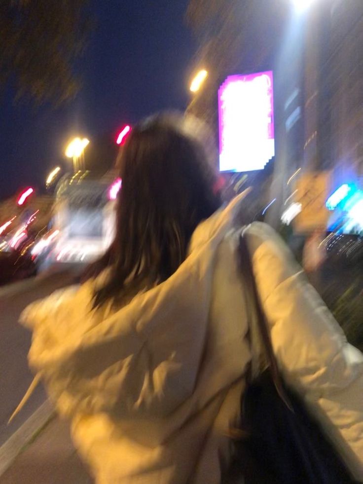 a woman is walking down the street at night