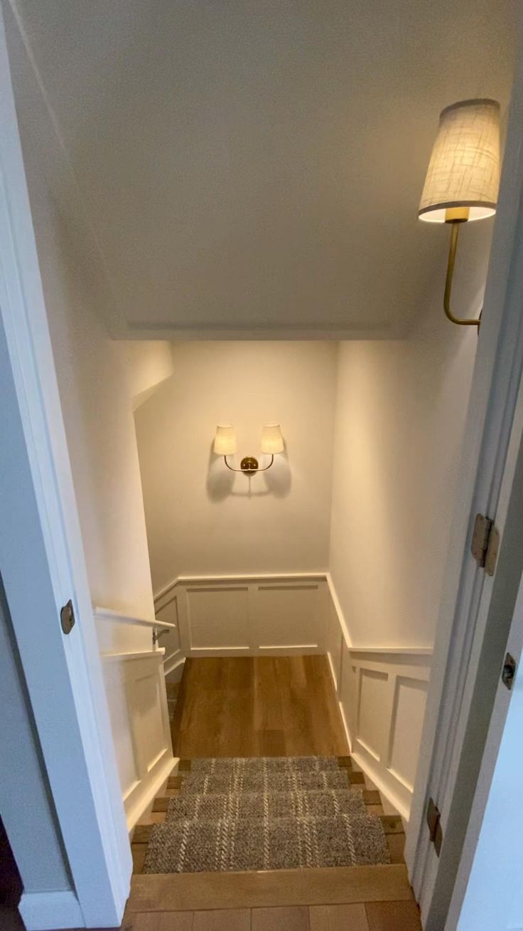 an empty hallway with wooden floors and two lights on either side of the door way