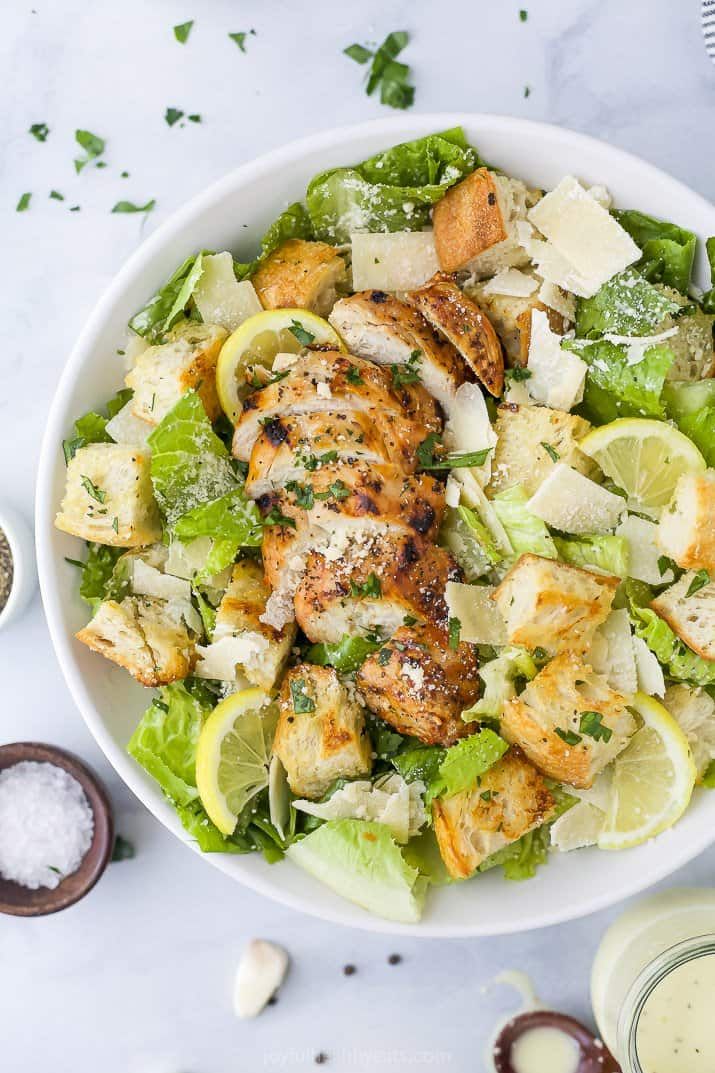 a white bowl filled with chicken, lettuce and lemon wedges on top of a table