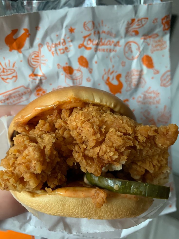 a fried chicken sandwich with pickles and ketchup on a paper wrapper