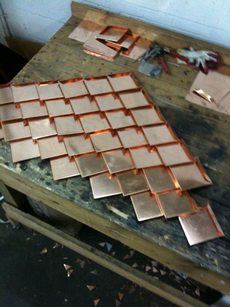 some copper tiles are sitting on a table with other metal parts around them and one is laying on the floor