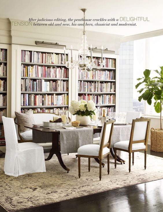 a dining room table with chairs and bookshelves in the background, surrounded by white linens