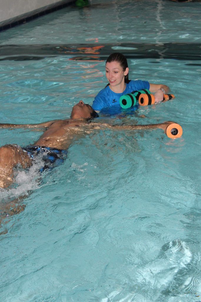 two people swimming in a pool with water wheels attached to their backs and arms, one person holding an orange frisbee