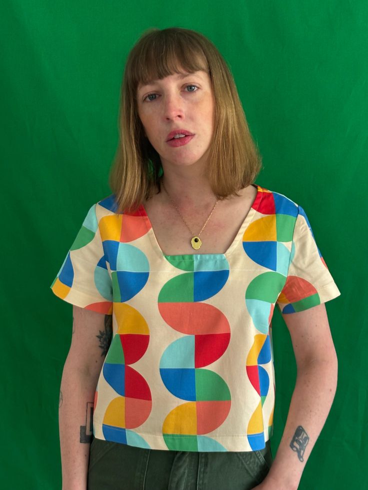 a woman standing in front of a green background wearing a colorful shirt with circles on it