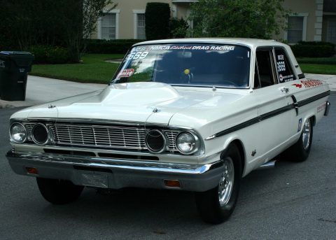 an old white car parked in front of a house on the side of the road